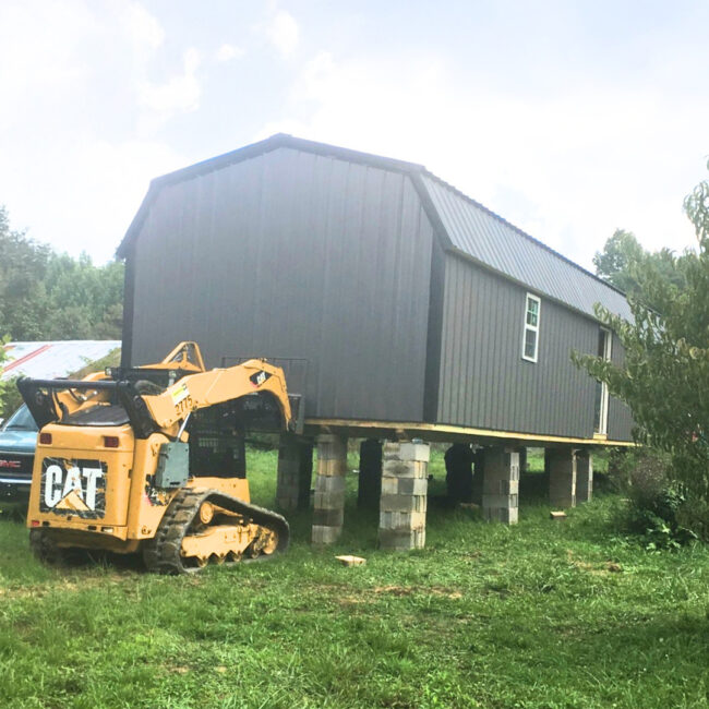 Skid-steer placing Barn Shed on elevated foundation